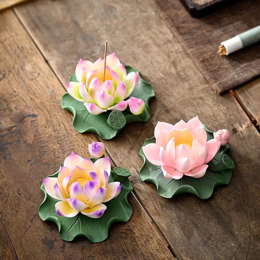 Three artisan lotus ceramic incense burners in different colors on vintage wooden table with incense supplies