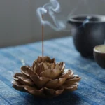 Handcrafted lotus-shaped ceramic incense burner with lit incense and rising aromatic smoke on traditional tea table