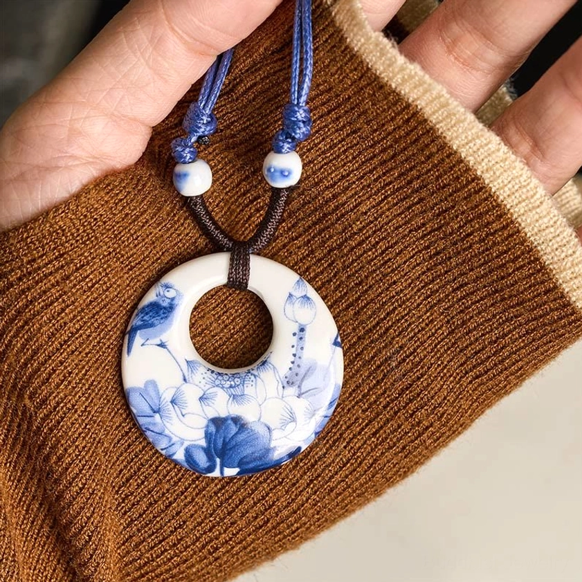 Close-up handheld Buddhist lotus pendant with lotus and bird printed design on brown sweater background
