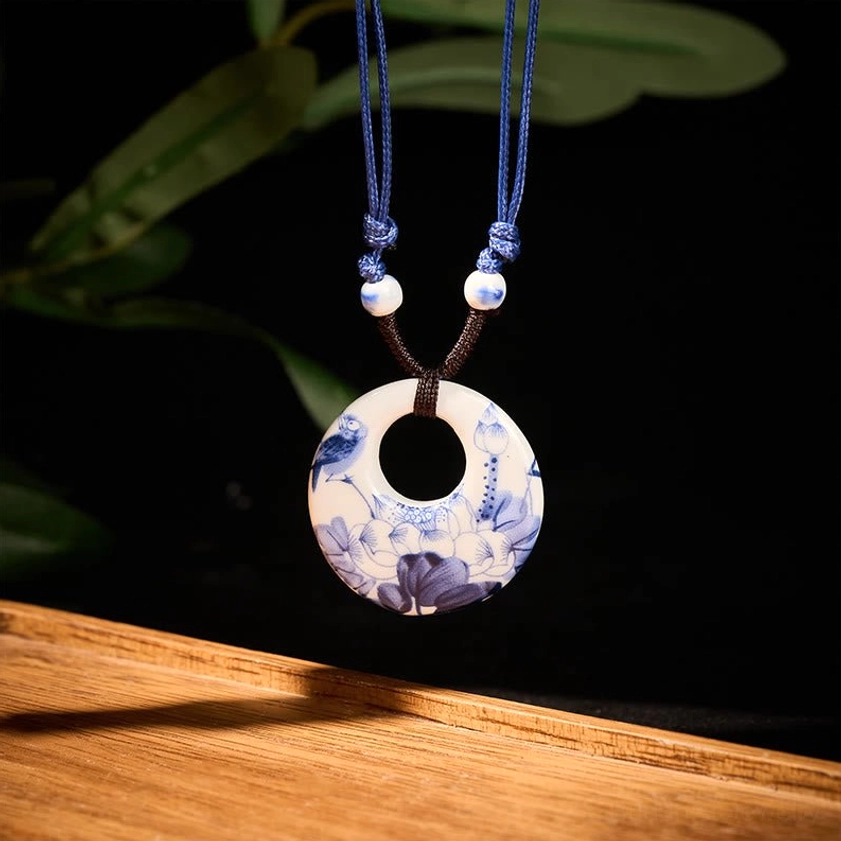 Buddhist lotus pendant necklace hanging frontal view showing bird and lotus floral pattern on dark background