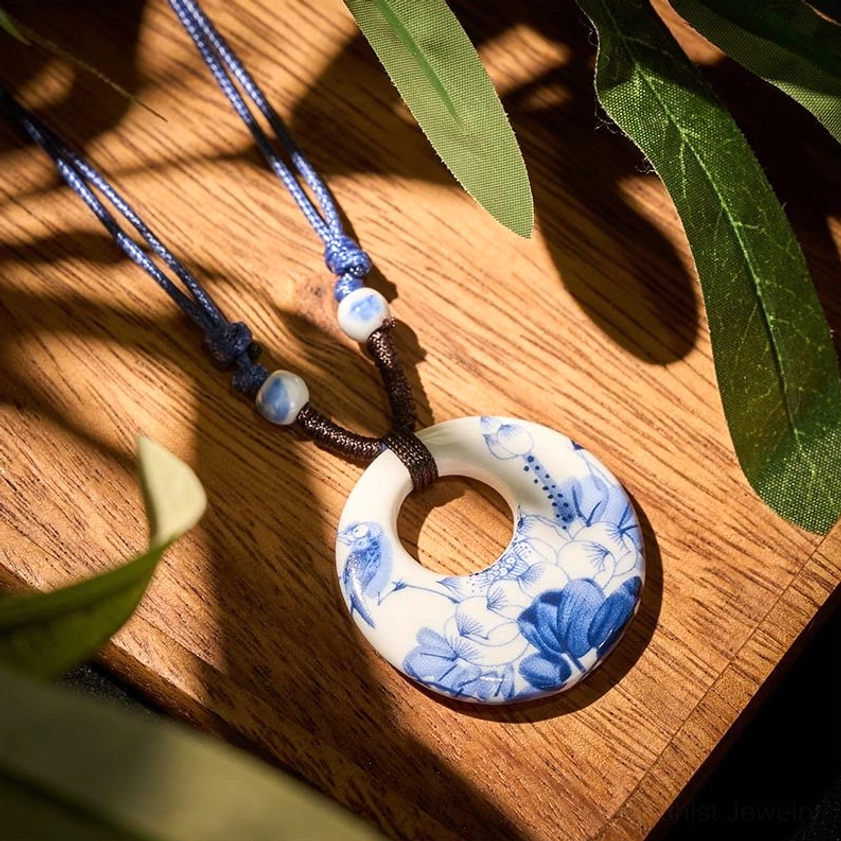 Blue and white ceramic lotus pendant necklace with woven rope, overhead view showing floral design on wooden table