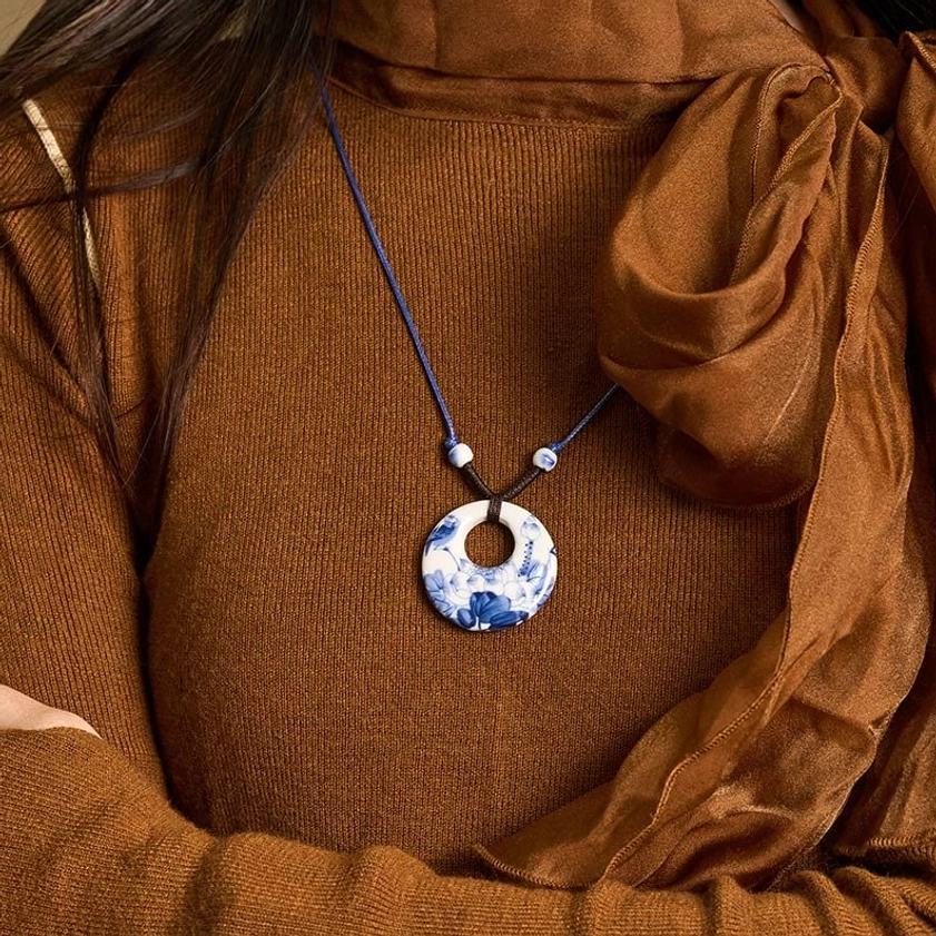 Blue and white ceramic lotus pendant necklace worn as upper body close-up with brown knit top and silk scarf