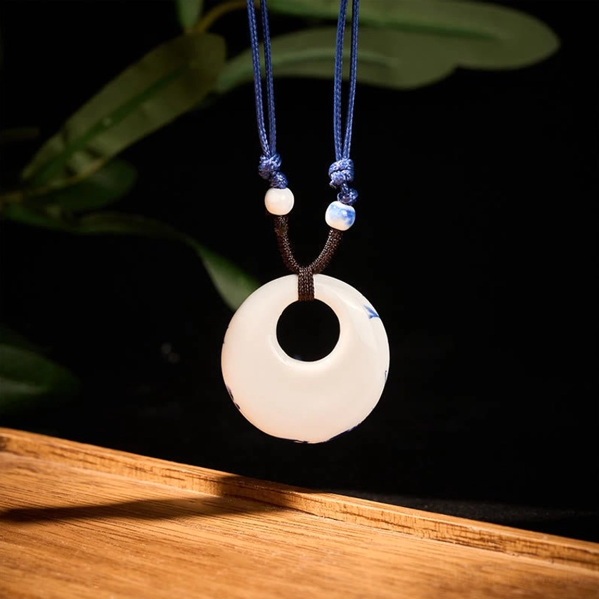 Plain white ceramic lotus pendant necklace side view with tiny blue decorative beads on natural rope