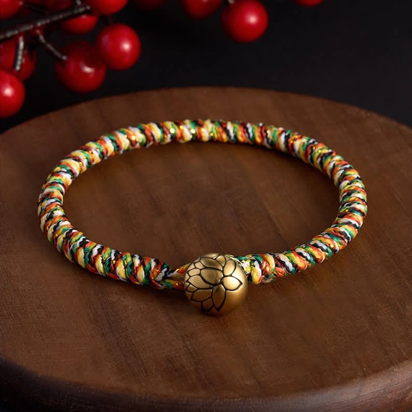 Multicolor woven lotus charm bracelet with copper lotus-shaped pendant on wooden coaster with red berry decoration