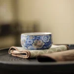 Gilt blue and white porcelain tea cup with lotus chrysanthemum plum blossom design side view on dark tea tray