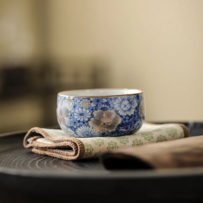 Gilt blue and white porcelain tea cup with lotus chrysanthemum plum blossom design side view on dark tea tray
