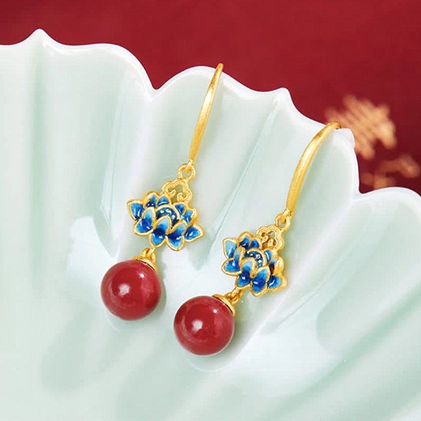 Lotus drop earrings with cinnabar pendants and gold ear posts on green ceramic tray - top down product shot