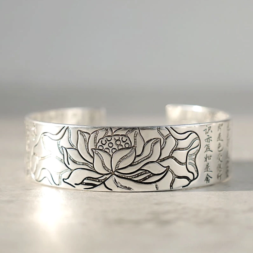 Open cuff lotus bracelet white copper front flat view with large carved lotus motif and edge sutra text on gray background