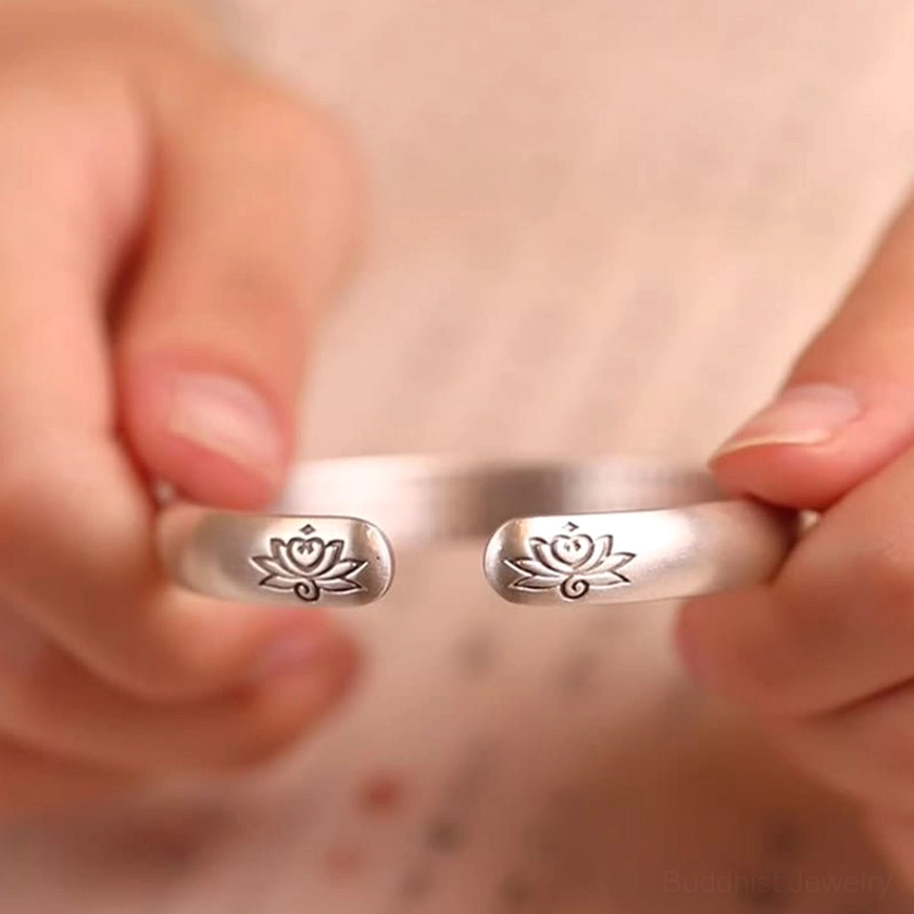 Open cuff bangle front flat view displaying two lotus engravings on cuff ends with hand-held display