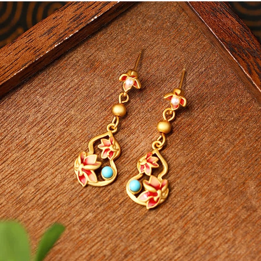 Top-down side view of turquoise lotus enamel drop earrings showing matte gold finish, vibrant red enamel lotus motifs, and turquoise stone inlays on wooden surface