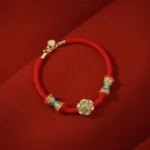 Sterling silver lotus drum charm with red cord bracelet, top-down side view showcasing enamel details on dark velvet