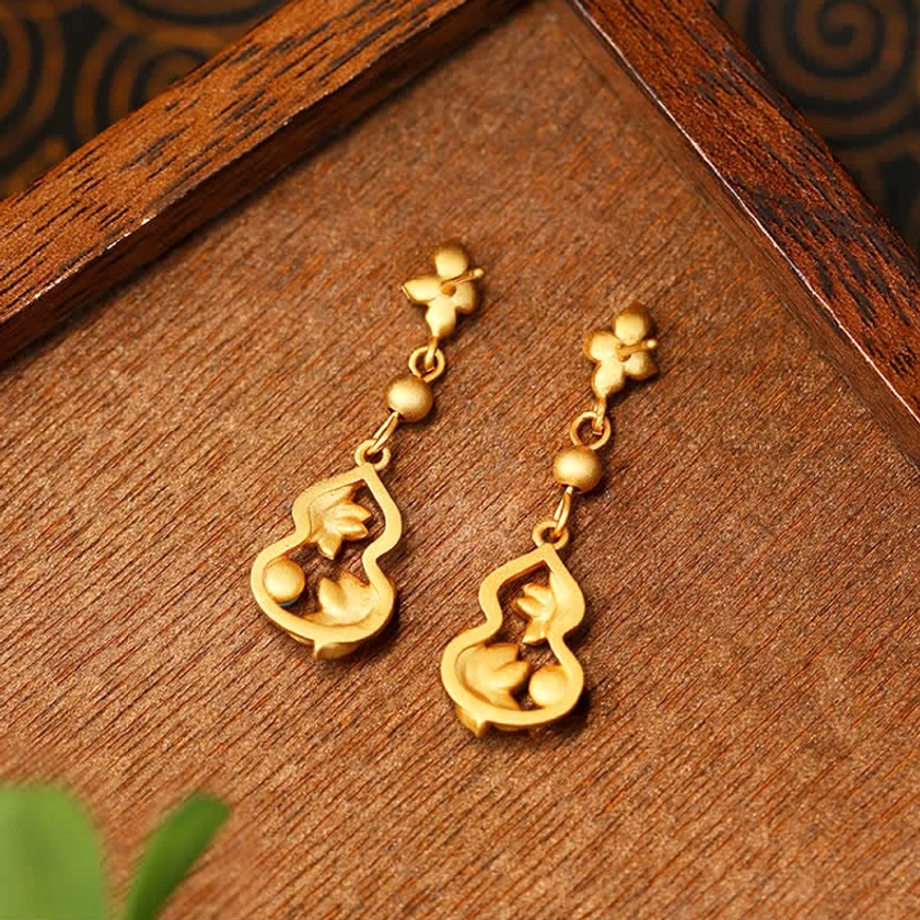 Flat lay of plain lotus gourd drop earrings with matte gold tone and flower ear posts on wooden display surface, detail perspective of Buddhist spiritual jewelry