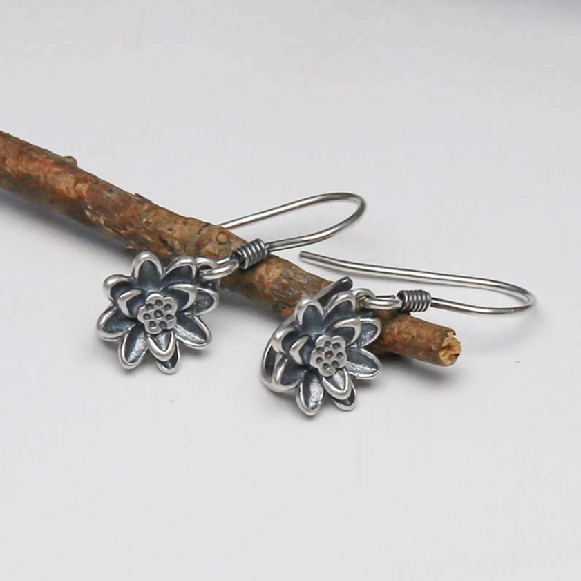 Pair of antique silver lotus flower earrings displayed flat on wooden branch, top side angle view