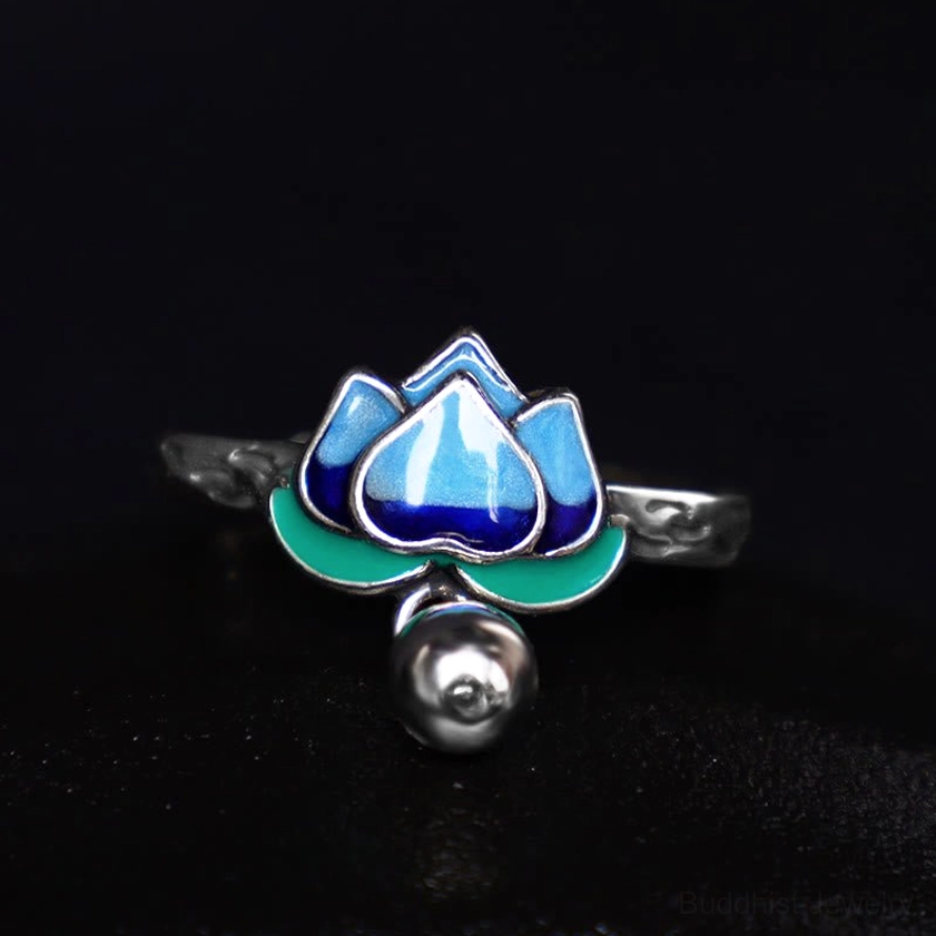Cloisonné lotus ring featuring vibrant blue enamel petals and silver bell pendant against dark background, top-down product view