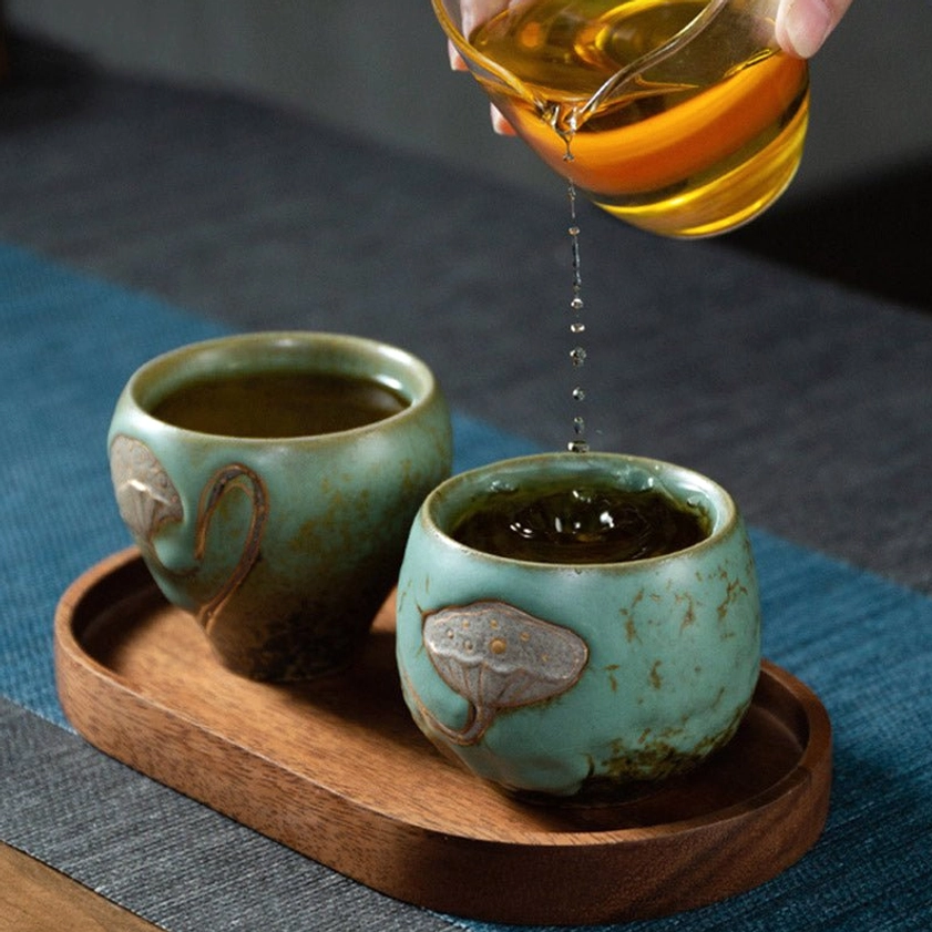 Two matching turquoise ceramic tea cups on wooden serving tray with brewed tea, overhead brewing scene
