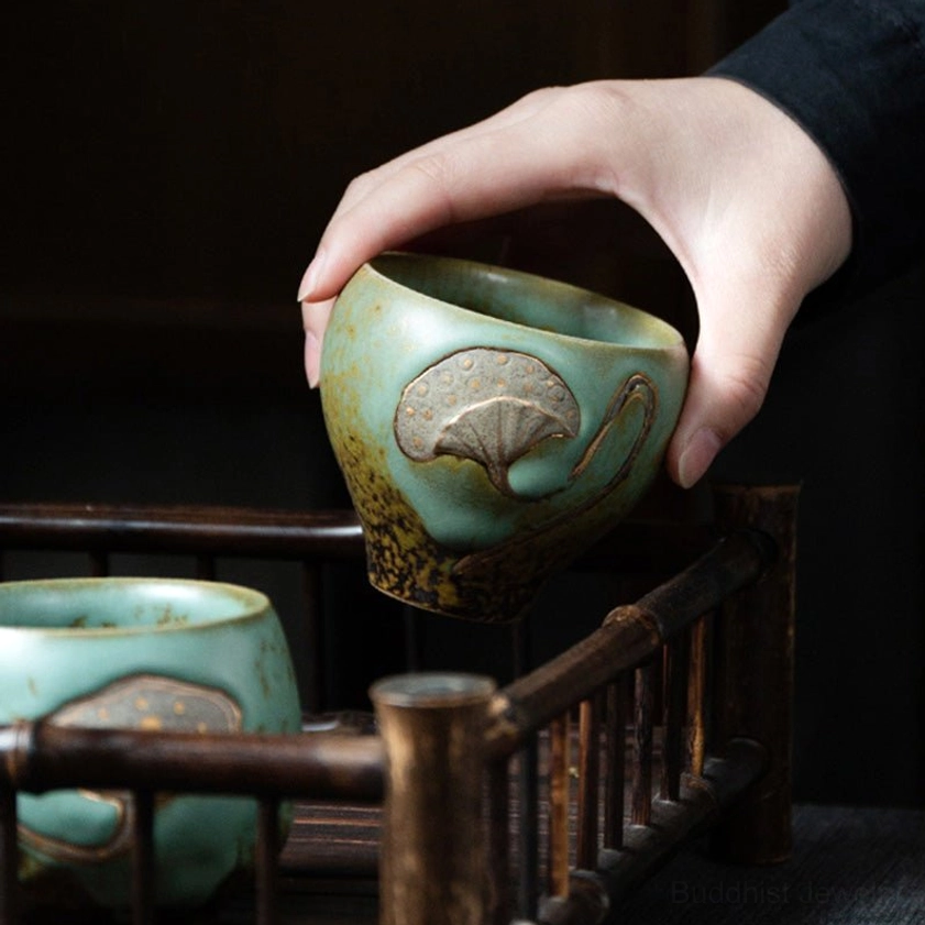 Hand holding turquoise lotus pod engraved ceramic teacup with brown lower glaze, side close-up detail