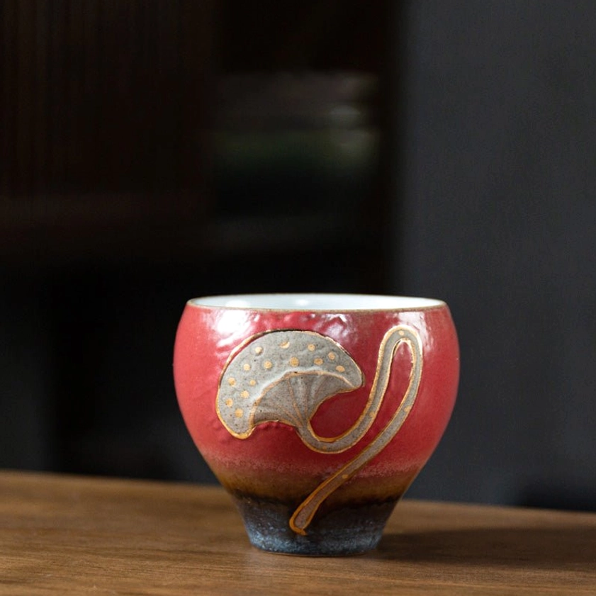 Red gradient glazed lotus engraved ceramic teacup with white interior and embossed pattern detail