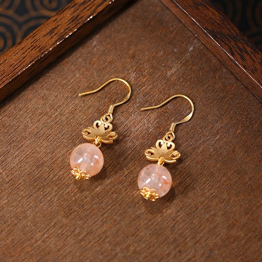 Buddhist lotus symbol enamel drop earrings with natural citrine stone and gold accents, wooden table display