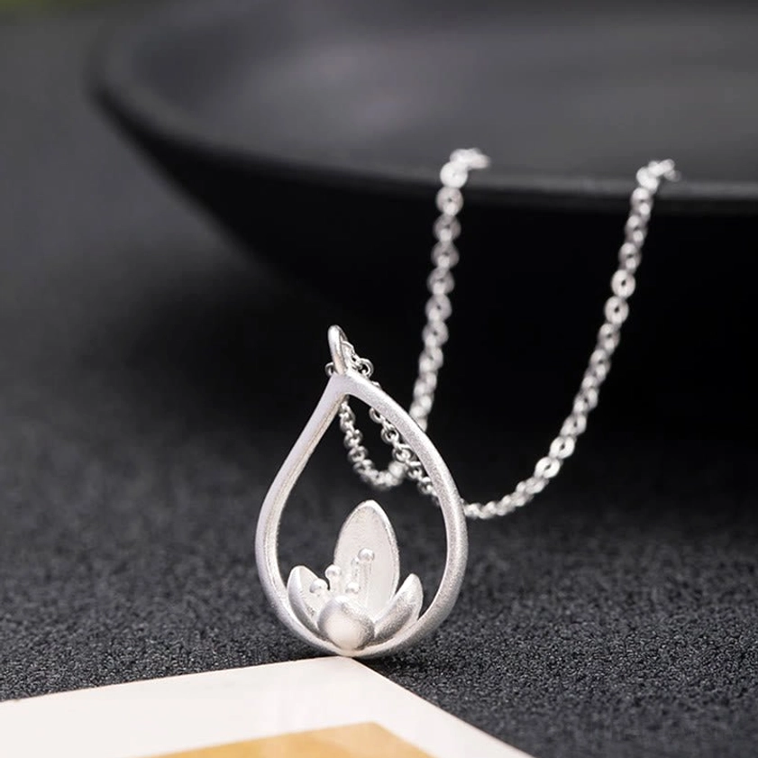 Sterling silver lotus necklace tilted pendant view with draped chain, front close-up displaying smooth matte finish and pendant details