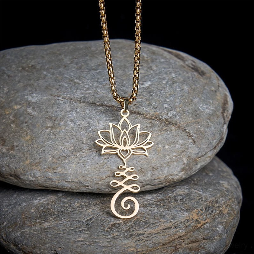 Gold-toned lotus enlightenment pendant necklace with hollow carved Buddhist symbol, displayed from top-down angle on grey stones