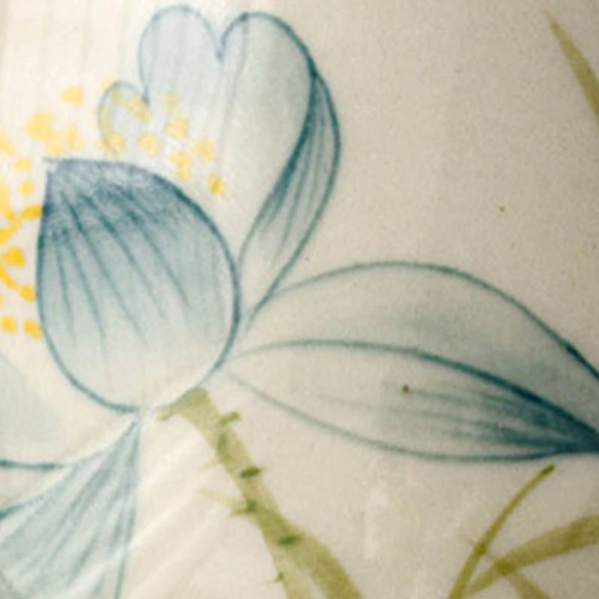 Macro close-up of hand-painted lotus flower with blue petals, yellow stamens, and green leaves on ceramic surface
