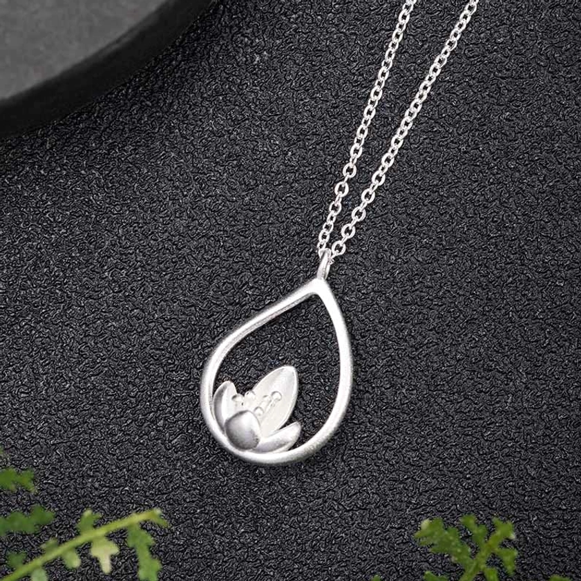 Buddhist lotus necklace pendant in sterling silver, side profile view displaying delicate cable chain and three-dimensional lotus flower detail against black background