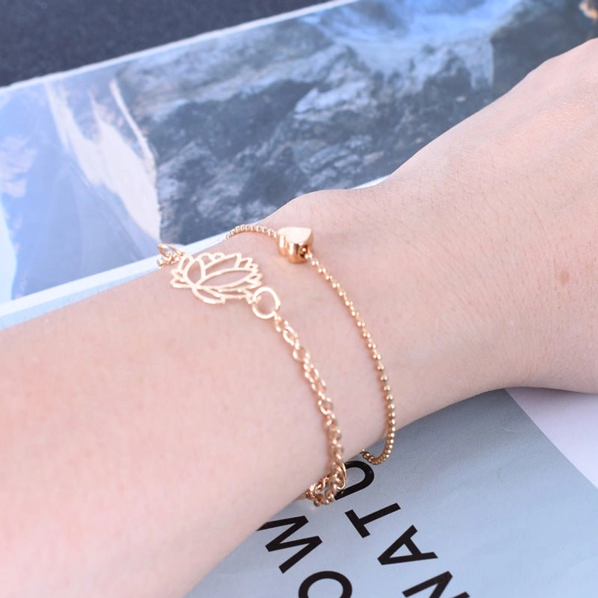 Close-up forearm view of lotus and heart charm bracelets showing delicate link chain design