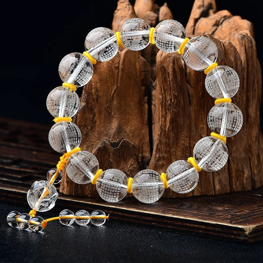 White crystal Buddhist bracelet with Lotus and Heart Sutra design, side profile view on wooden stump, featuring round engraved beads and yellow cord knots with crystal charms
