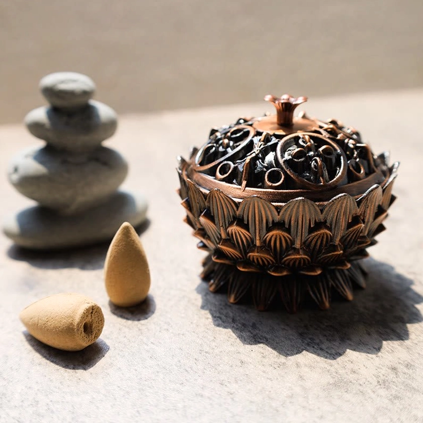 Lotus flower incense burner bronze finish displayed on stone table with stacked rocks and backflow incense cones