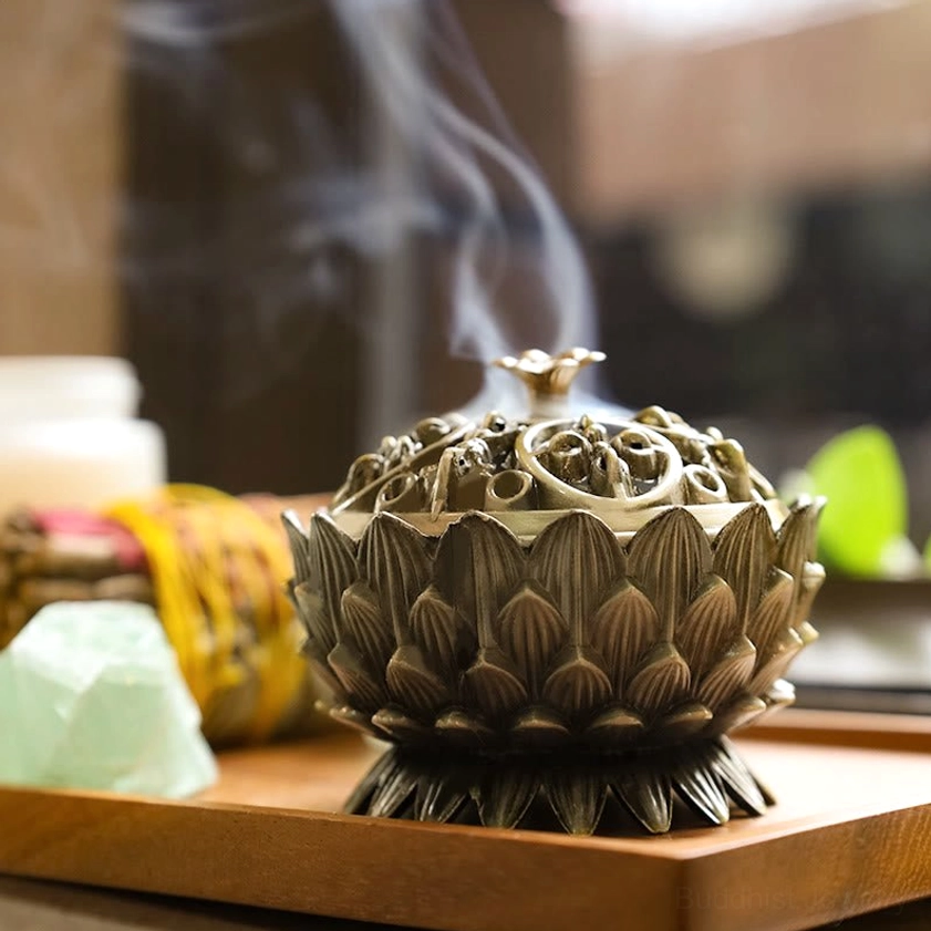 Bronze lotus incense burner eye-level side view with rising smoke and hollow carved lid on wooden spiritual display