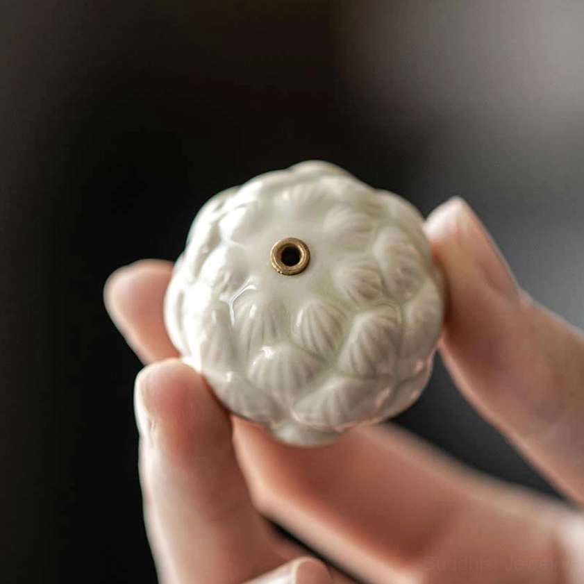 Detailed close-up of white glazed lotus ceramic incense burner showing intricate lotus relief texture and central incense socket, held in hands