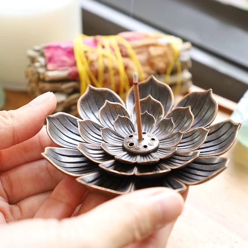 Hand-held lotus incense burner with single incense stick inserted, held in two palms on wooden surface