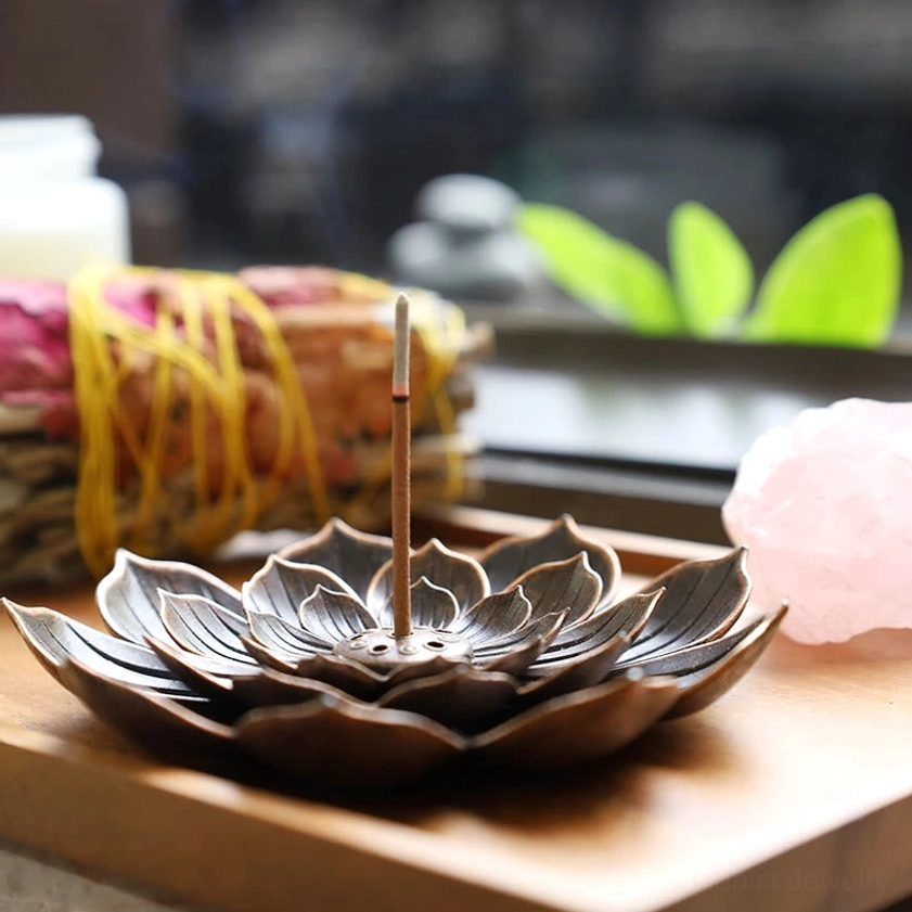 Lotus-shaped incense burner with inserted incense stick arranged on wooden tray with home decor elements