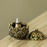 Overhead view of handcrafted mini lotus copper incense burner with cone incense and separated carved lid on wooden surface