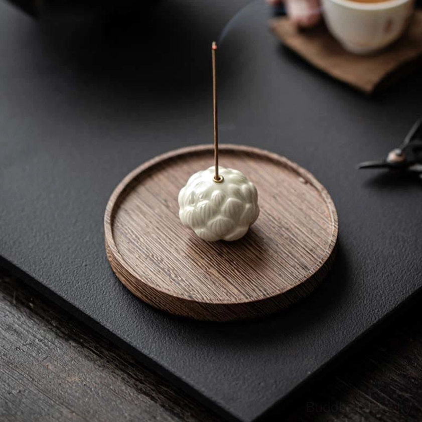 Overhead view of ceramic lotus incense holder with burning incense emitting fragrant smoke, tea cup coaster nearby