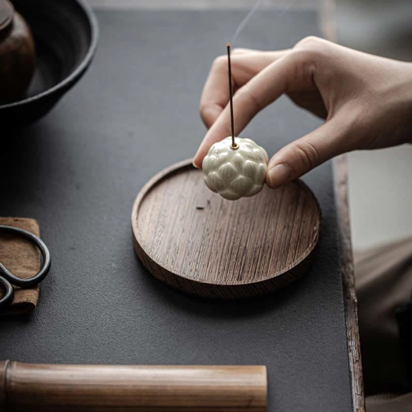 Hand placing ceramic lotus incense holder onto round wooden tray with scissors visible in background