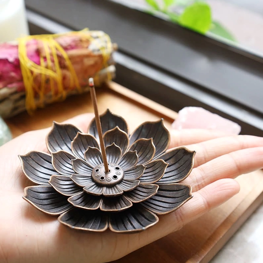 Lotus incense burner held in single palm on wooden windowsill with natural light, aged bronze finish