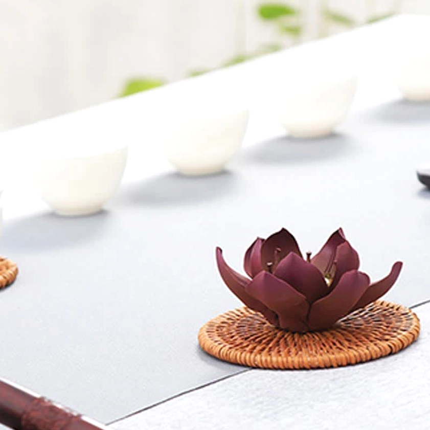 Lotus-shaped incense burner on brown rattan coaster showing three-quarter view with light gray tabletop styling
