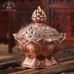 Red bronze Buddhist lotus incense burner with carved lid and flame finial, showing intricate hollow relief patterns and smoking incense