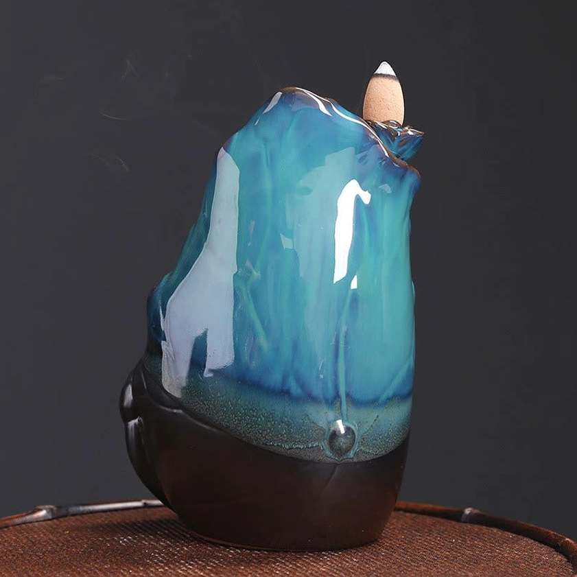 Side profile view of ceramic lotus backflow incense burner holding two backflow incense cones with gradient teal glaze