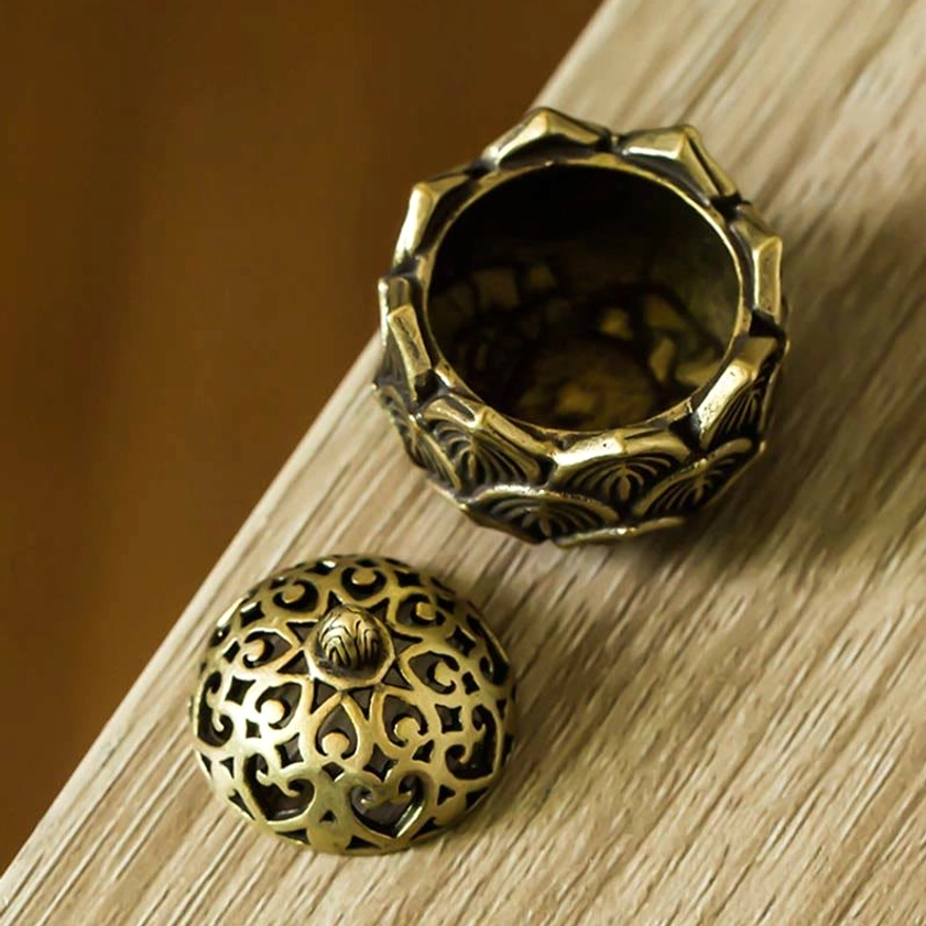 High side perspective of handcrafted lotus copper incense holder with textured base and separated lid on warm wooden desk