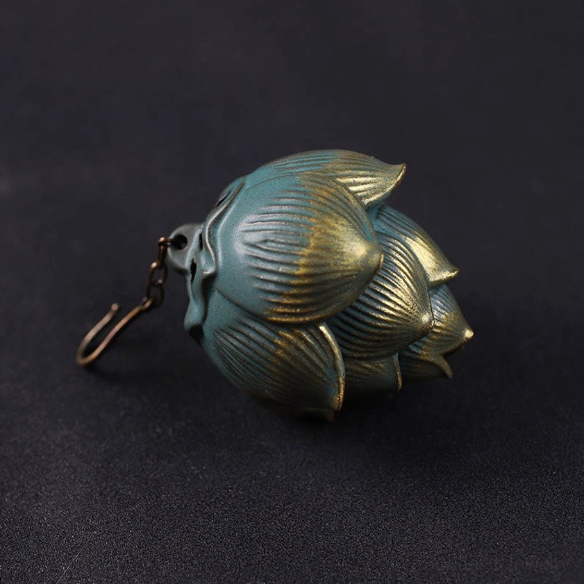 Bronze-green lotus incense burner with gold accents and hanging hook, right side flat lay view on dark tabletop