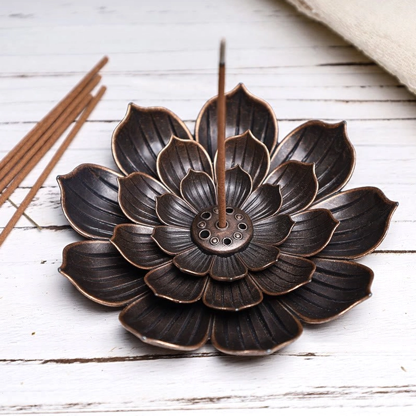 Bronze lotus incense holder displayed on white wood table with incense sticks, slightly elevated front view
