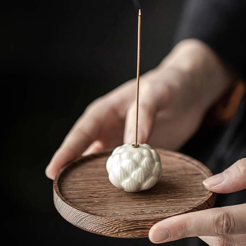 Close-up view of hands adjusting burning incense stick in smooth glazed ceramic lotus burner