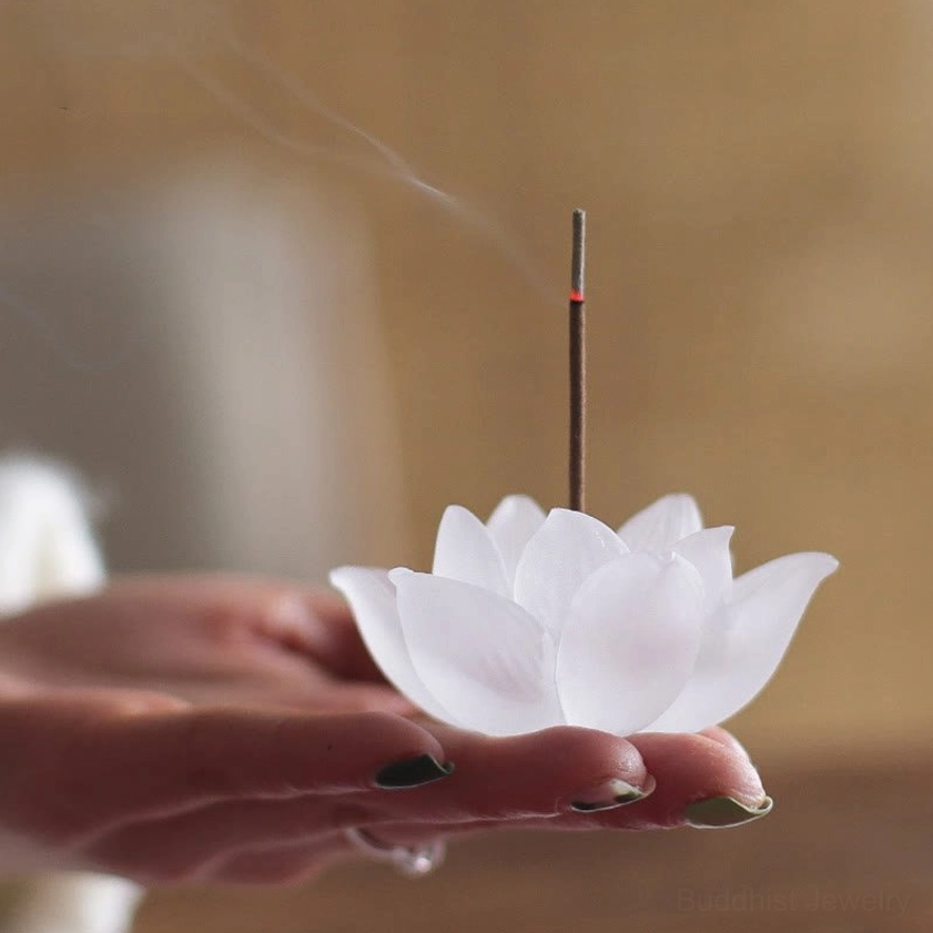 White frosted glass lotus incense burner held in fingertips with burning incense warm indoor setting