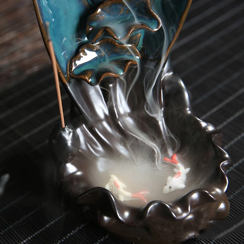 Close-up top view of lotus backflow incense holder showing two decorative painted koi fish on dark brown ruffled ceramic tray with visible incense smoke