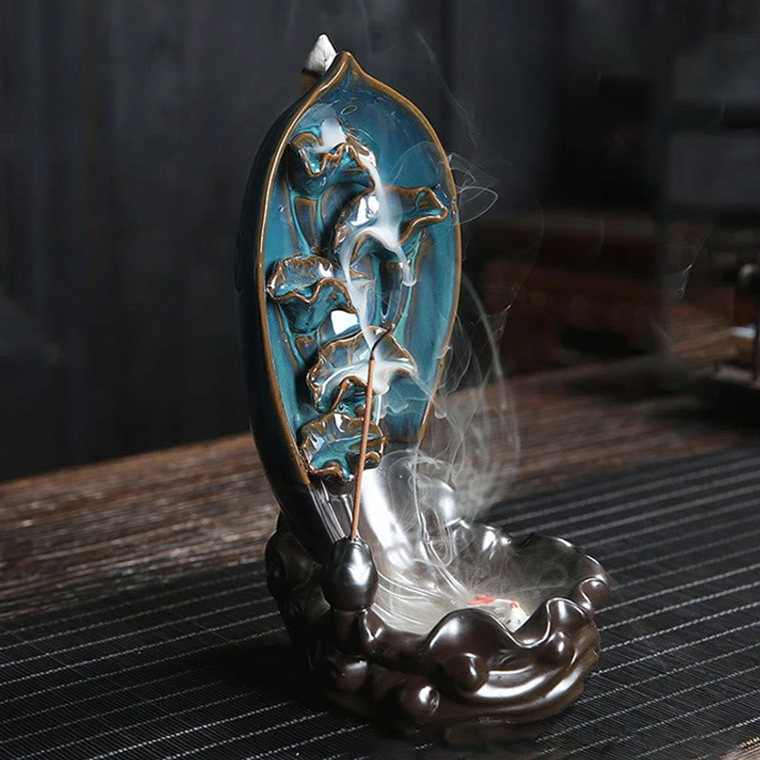 Lotus backflow incense holder with decorative koi fish tray showing cascading incense smoke on striped wooden table