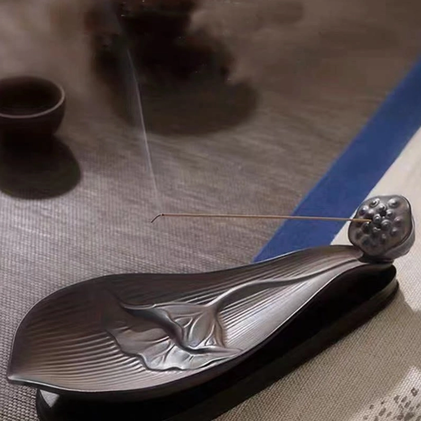 Low angle view of brown ceramic lotus pod incense holder with striped body on table with tea set