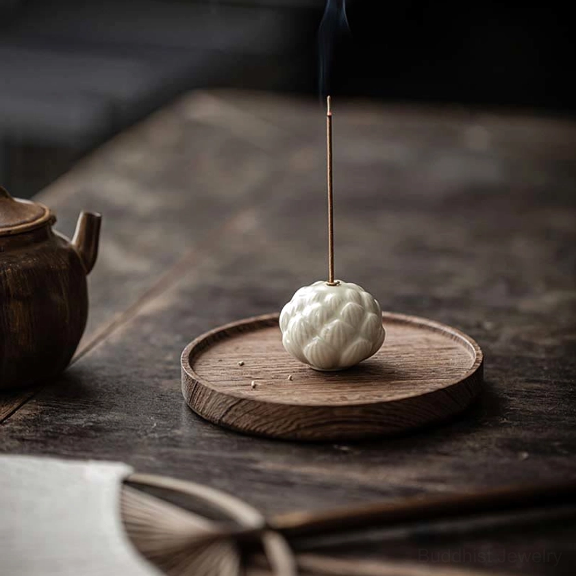 Ceramic lotus incense burner with burning incense on traditional Chinese wooden tea table with teapot in background