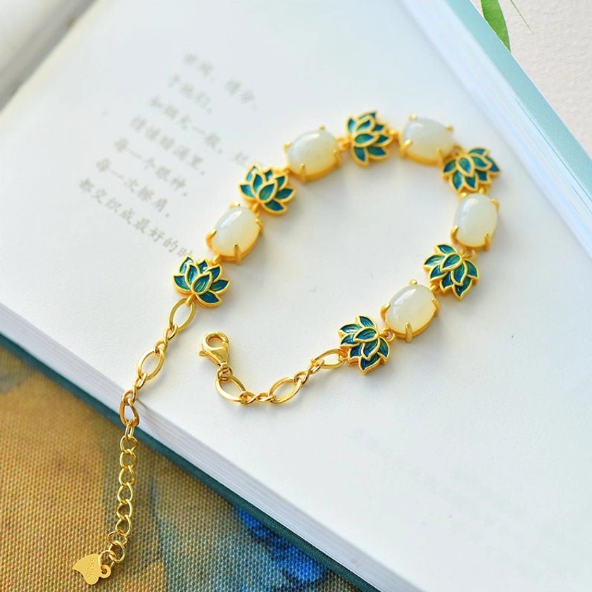 Adjustable lotus jade bracelet side view showing the extension chain and alternating jade beads with lotus charm details on an open book